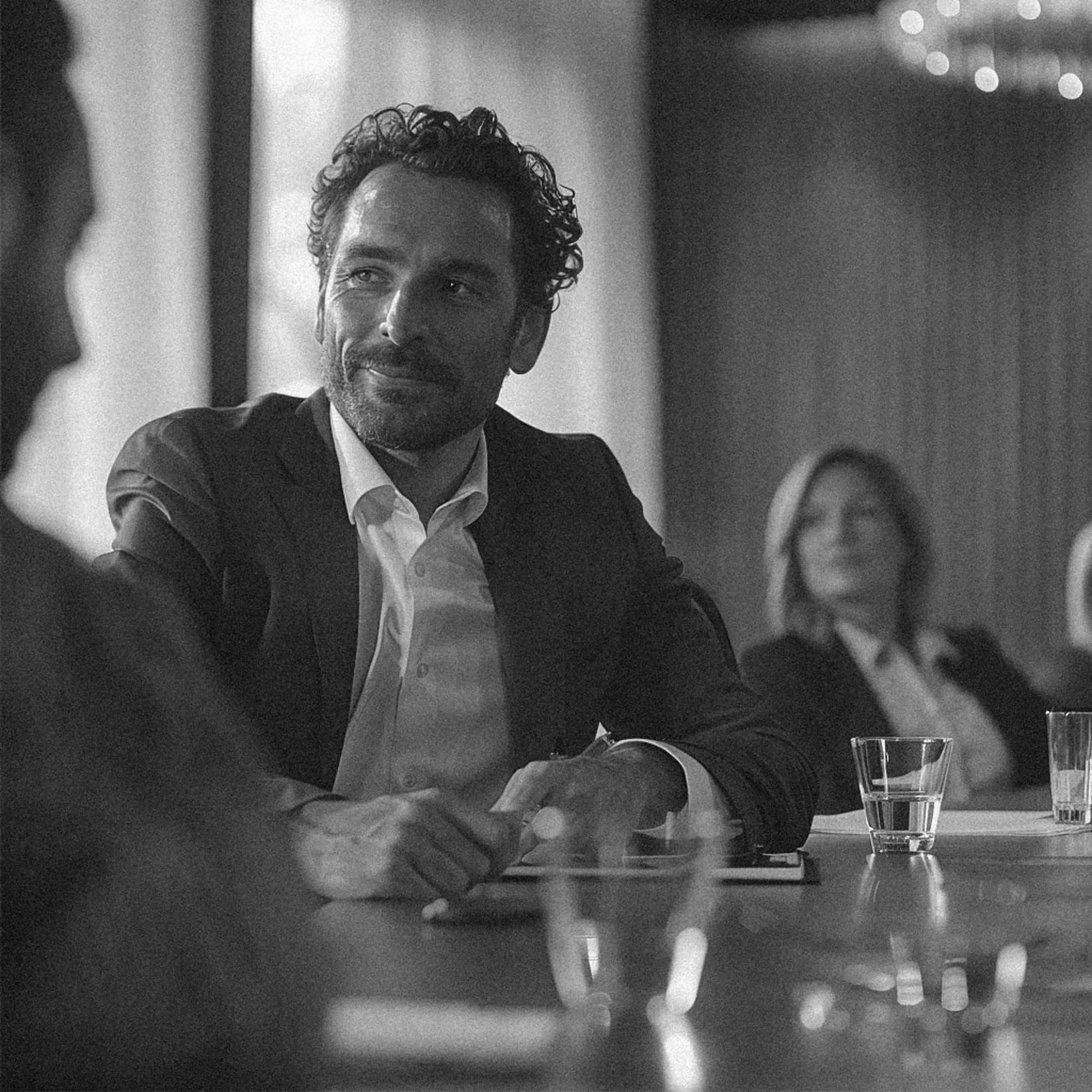a man sitting at a table with other people in the background